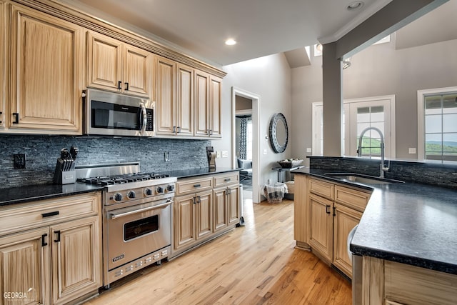 kitchen with stainless steel appliances, tasteful backsplash, dark stone countertops, sink, and light wood-type flooring