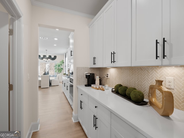 interior space featuring white cabinetry, backsplash, crown molding, and light hardwood / wood-style floors