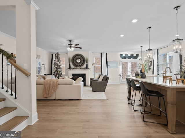 living room featuring crown molding, sink, ceiling fan with notable chandelier, and light hardwood / wood-style flooring