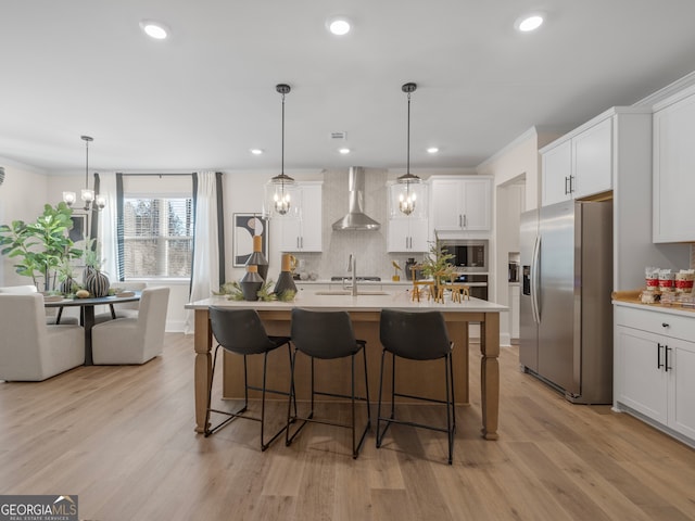 kitchen featuring built in microwave, wall chimney range hood, decorative light fixtures, and stainless steel refrigerator with ice dispenser