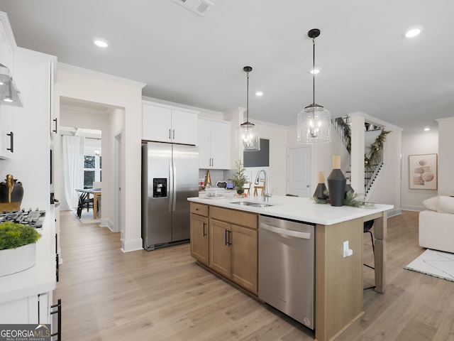 kitchen featuring sink, white cabinetry, stainless steel appliances, a center island with sink, and decorative light fixtures