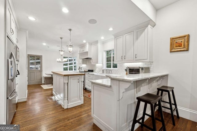 kitchen with appliances with stainless steel finishes, a breakfast bar, white cabinetry, hanging light fixtures, and a center island