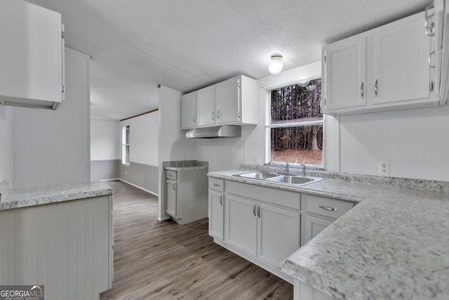 kitchen with kitchen peninsula, light hardwood / wood-style flooring, sink, white cabinets, and a textured ceiling