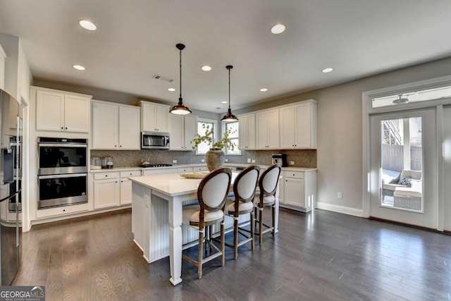 kitchen with a wealth of natural light, a kitchen island, white cabinetry, stainless steel appliances, and hanging light fixtures