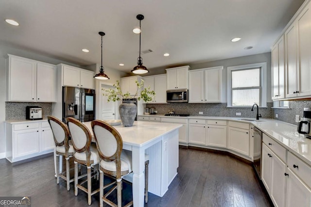 kitchen with a center island, appliances with stainless steel finishes, sink, decorative light fixtures, and white cabinets