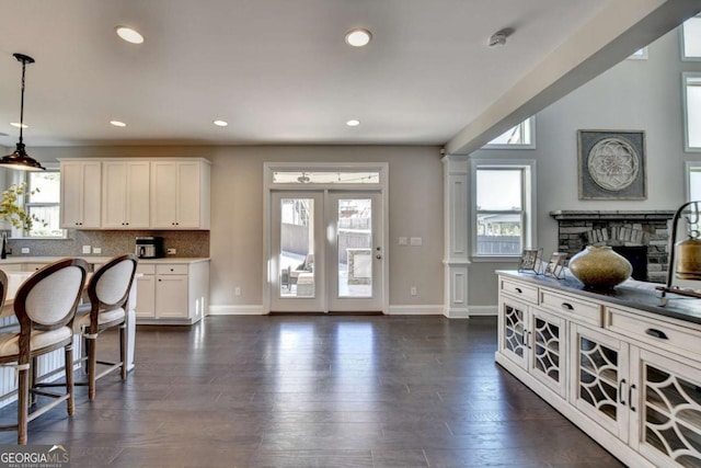 kitchen featuring white cabinetry, ornate columns, a fireplace, tasteful backsplash, and hanging light fixtures