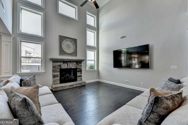 living room featuring ceiling fan, a stone fireplace, a high ceiling, and dark wood-type flooring