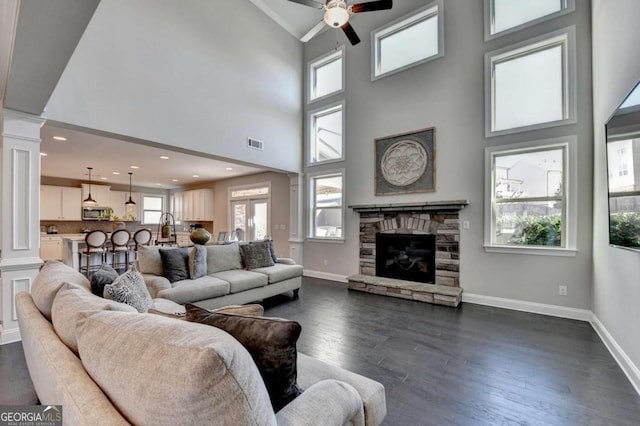 living room with dark hardwood / wood-style flooring, a stone fireplace, ceiling fan, high vaulted ceiling, and decorative columns