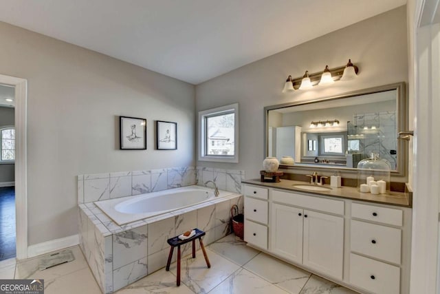 bathroom featuring plenty of natural light, a relaxing tiled tub, and vanity