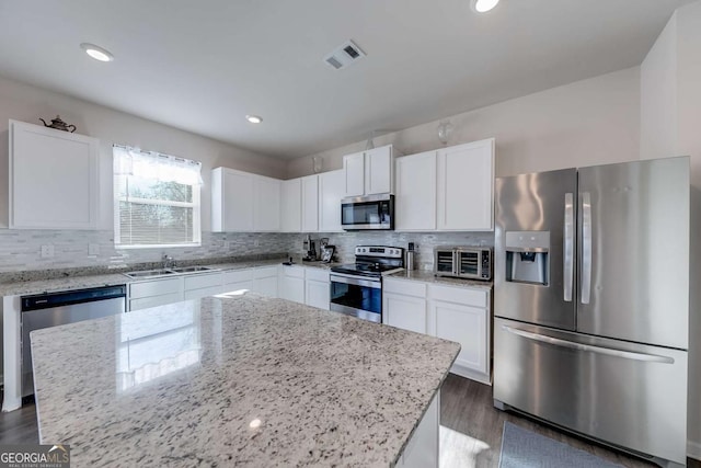 kitchen with light stone countertops, appliances with stainless steel finishes, a center island, white cabinetry, and sink