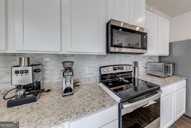 kitchen featuring stainless steel appliances, white cabinetry, light stone counters, and tasteful backsplash