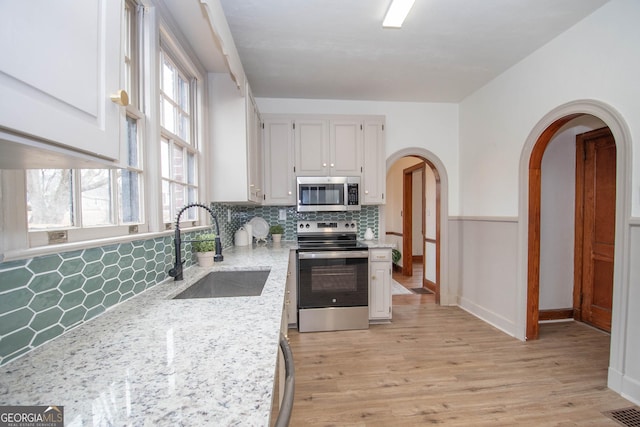 kitchen featuring white cabinets, stainless steel appliances, a healthy amount of sunlight, decorative backsplash, and sink