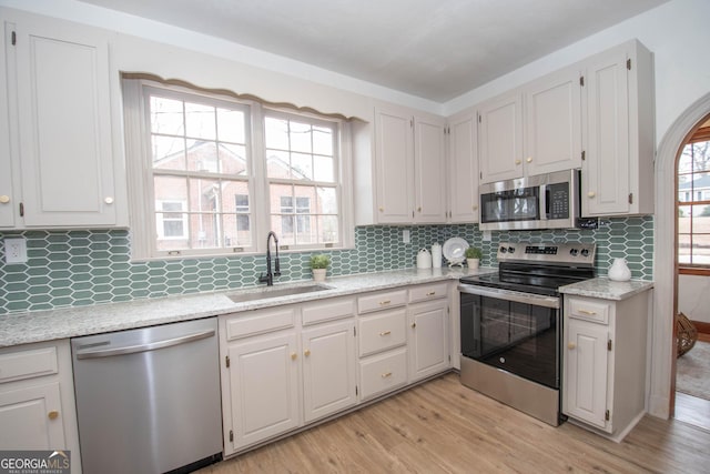 kitchen with white cabinets, appliances with stainless steel finishes, a healthy amount of sunlight, sink, and light hardwood / wood-style flooring