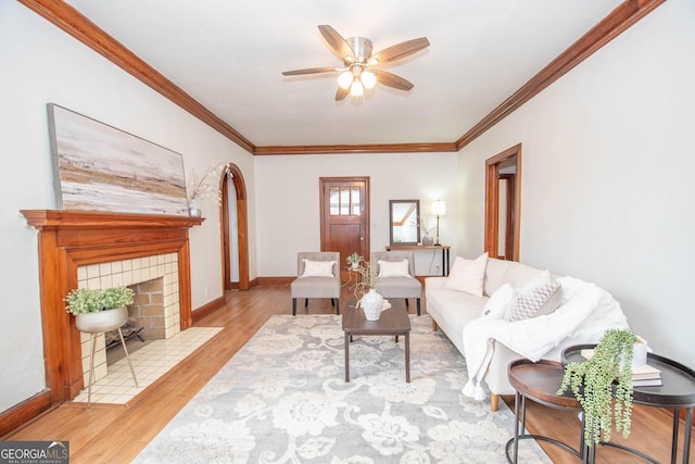 living room with ceiling fan, a fireplace, ornamental molding, and light wood-type flooring