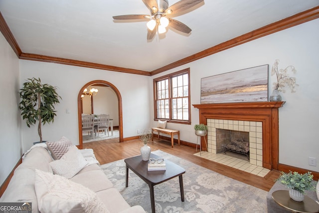 living room featuring crown molding, light hardwood / wood-style floors, ceiling fan with notable chandelier, and a fireplace