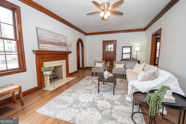 living room with ceiling fan, crown molding, light hardwood / wood-style floors, and a tile fireplace