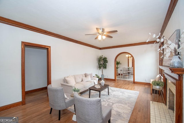 living room with light wood-type flooring, ceiling fan, ornamental molding, and a tile fireplace