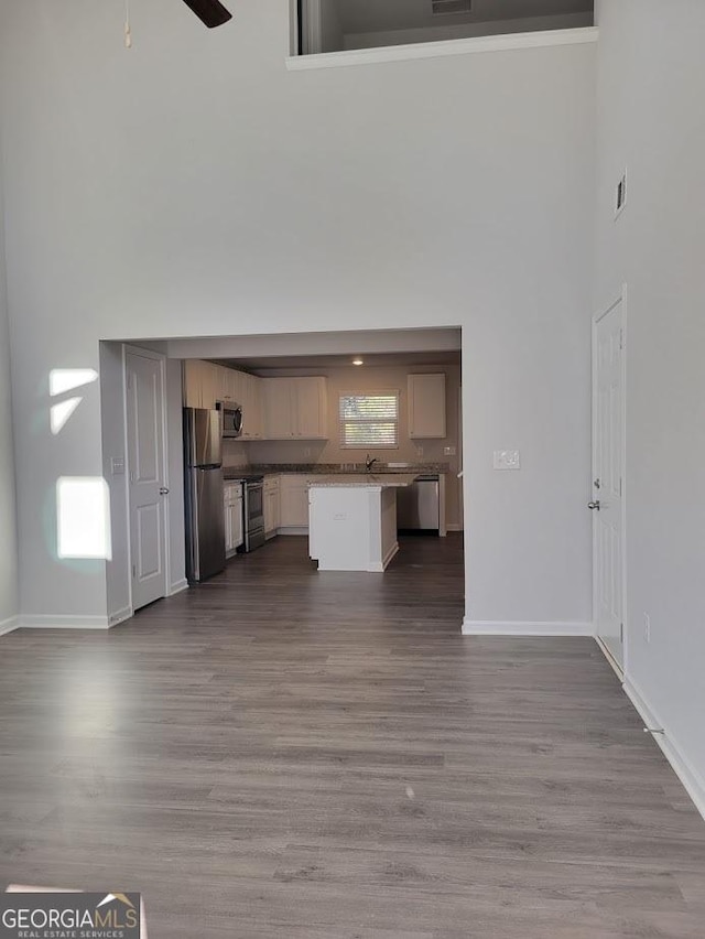 unfurnished living room featuring ceiling fan, wood-type flooring, and a towering ceiling