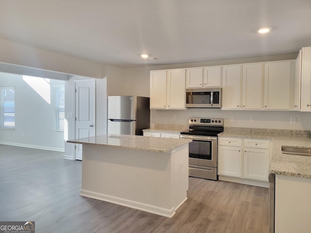 kitchen with white cabinets, a center island, stainless steel appliances, and light wood-type flooring