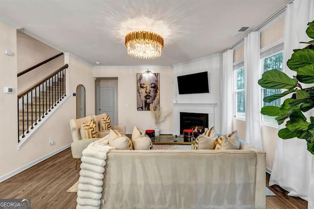 living room with wood-type flooring, crown molding, and an inviting chandelier