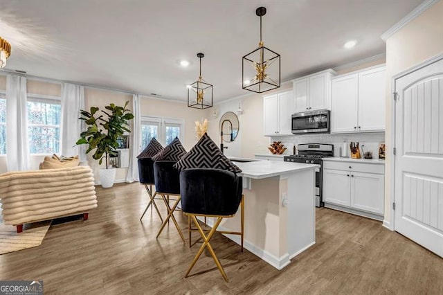 kitchen with crown molding, decorative light fixtures, white cabinets, a breakfast bar, and stainless steel appliances