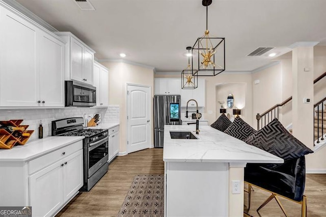 kitchen featuring light stone countertops, white cabinetry, decorative light fixtures, stainless steel appliances, and a center island with sink