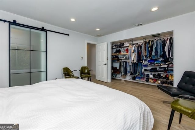 bedroom featuring hardwood / wood-style floors, crown molding, a closet, and a barn door