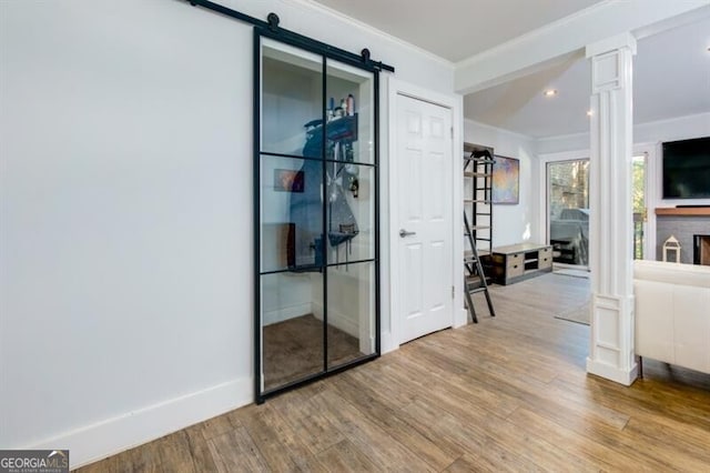 interior space with ornate columns, ornamental molding, a barn door, and light wood-type flooring