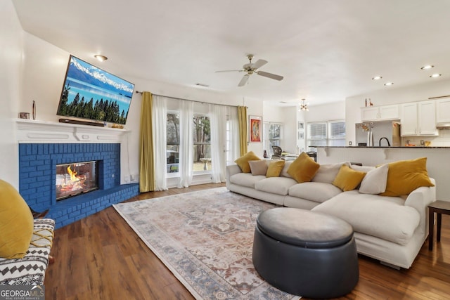 living room featuring ceiling fan, a wealth of natural light, dark hardwood / wood-style flooring, and a fireplace