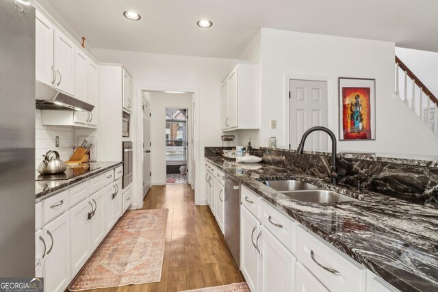 kitchen with white cabinetry, sink, dark stone countertops, light wood-type flooring, and stainless steel appliances