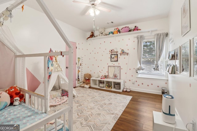 bedroom featuring hardwood / wood-style flooring, ceiling fan, and a crib