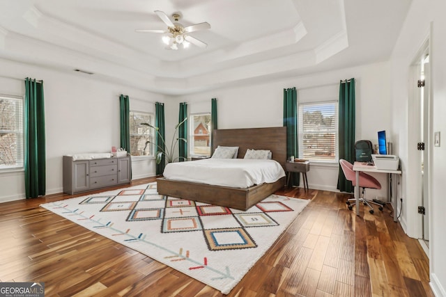 bedroom with ceiling fan, hardwood / wood-style flooring, and a tray ceiling