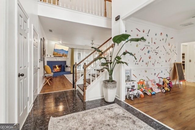 entrance foyer featuring ceiling fan, a brick fireplace, ornamental molding, and dark wood-type flooring