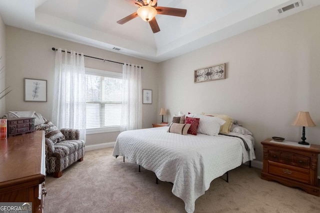 carpeted bedroom featuring ceiling fan and a tray ceiling