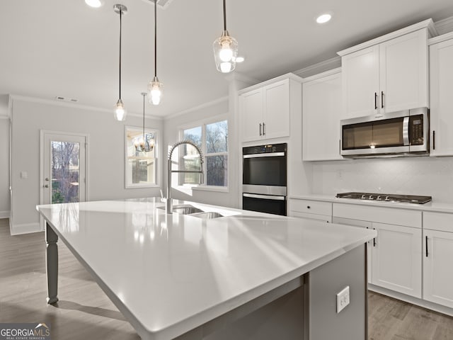kitchen with appliances with stainless steel finishes, an island with sink, hanging light fixtures, and white cabinets