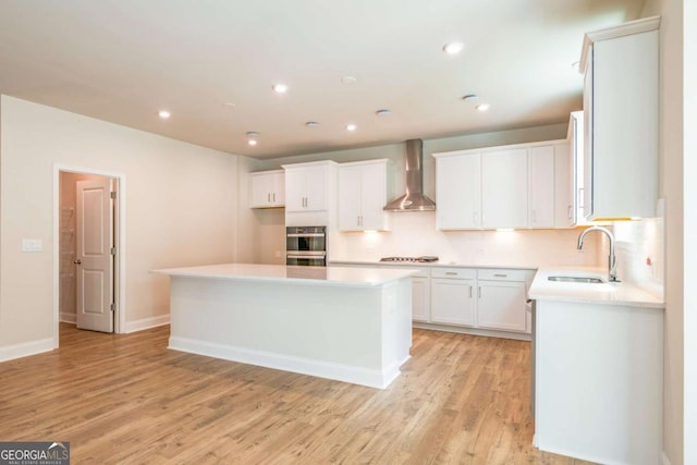 kitchen featuring light hardwood / wood-style floors, white cabinetry, sink, a kitchen island, and wall chimney exhaust hood