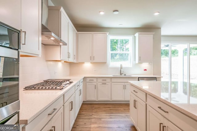 kitchen with sink, wall chimney range hood, white cabinets, and stainless steel gas stovetop