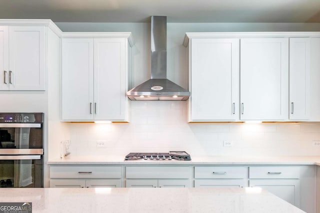 kitchen with white cabinets, wall chimney range hood, decorative backsplash, double wall oven, and stainless steel gas cooktop