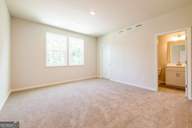 unfurnished bedroom featuring light colored carpet and ensuite bath