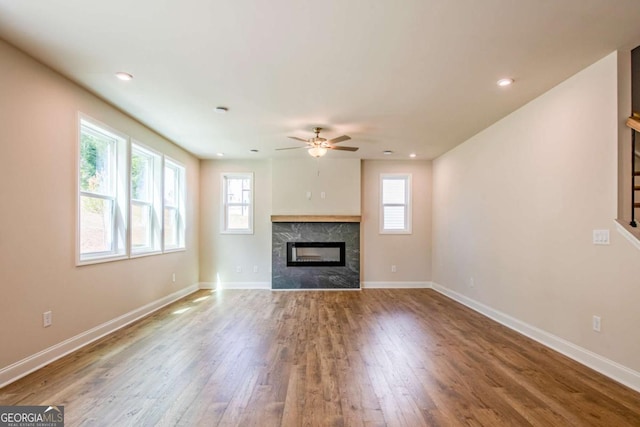 unfurnished living room featuring hardwood / wood-style flooring, a high end fireplace, and ceiling fan