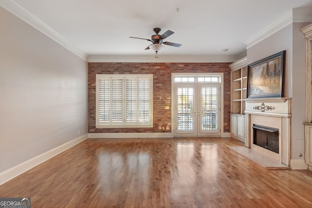 unfurnished living room with ornamental molding, brick wall, a high end fireplace, and hardwood / wood-style floors