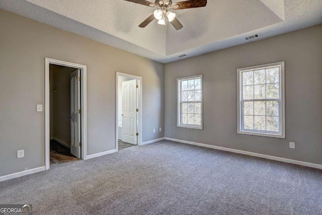 unfurnished bedroom featuring a spacious closet, a textured ceiling, multiple windows, a raised ceiling, and ceiling fan