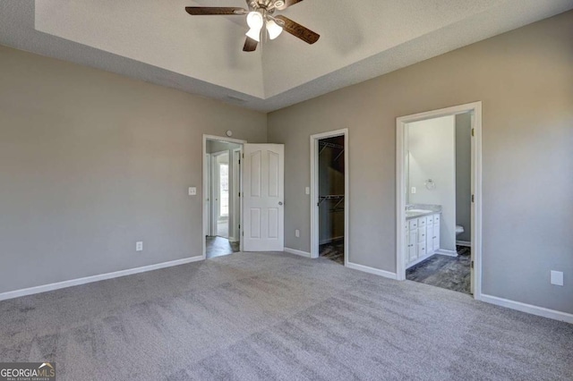 unfurnished bedroom featuring ceiling fan, carpet flooring, ensuite bath, a walk in closet, and a closet