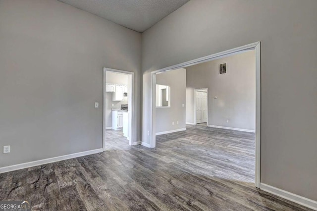 unfurnished room with a textured ceiling, dark hardwood / wood-style floors, and a towering ceiling