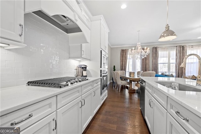 kitchen with appliances with stainless steel finishes, white cabinets, decorative light fixtures, sink, and wall chimney exhaust hood