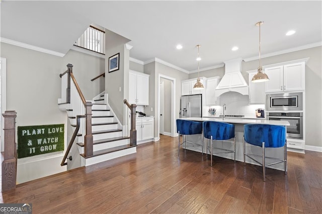 kitchen with appliances with stainless steel finishes, premium range hood, white cabinetry, pendant lighting, and an island with sink