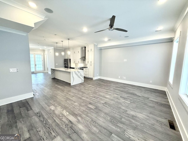 kitchen with pendant lighting, white cabinetry, sink, a center island with sink, and wall chimney range hood