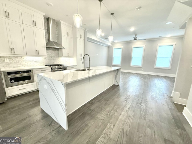 kitchen with sink, white cabinetry, a kitchen island with sink, stainless steel appliances, and wall chimney exhaust hood