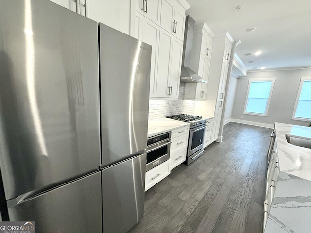 kitchen with stainless steel appliances, white cabinets, light stone counters, and wall chimney exhaust hood