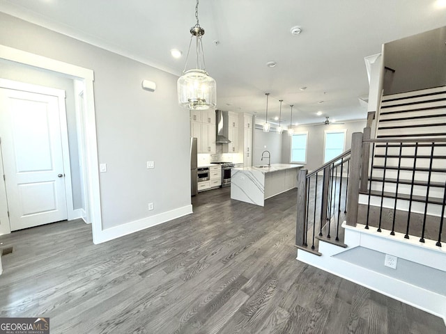 interior space with wall chimney exhaust hood, white cabinetry, dark hardwood / wood-style floors, pendant lighting, and a kitchen island with sink